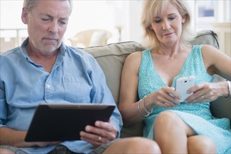 Portrait of couple sitting on sofa using digital tablet and smart phone