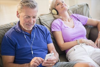 Portrait of couple sitting on sofa listening to music on headphones