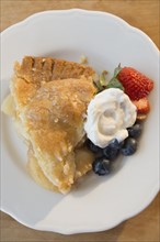 Close-up shot of portion of apple pie with fresh berries and cream on white plate