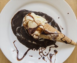 Studio shot of ice cream cone on plate with chocolate sauce