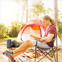 Man reading book in front of tent
