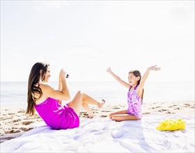 Mom taking picture of her daughter (6-7) on beach