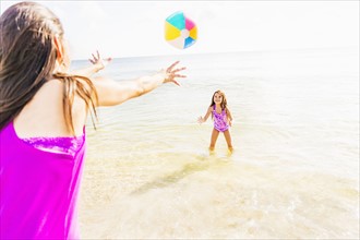 Mom throwing beach ball to her daughter (6-7) on beach