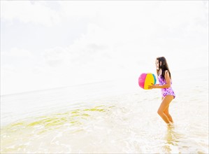 Side view of girl (6-7) holding beach ball on beach