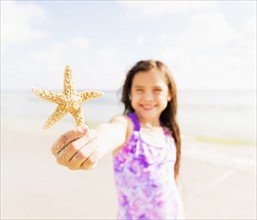 Portrait of girl (6-7) holding starfish on beach