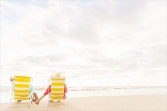 Rear view of couple sitting in lounge chairs on beach