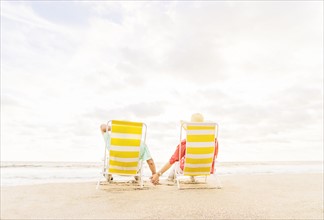 Rear view of couple sitting in lounge chairs on beach