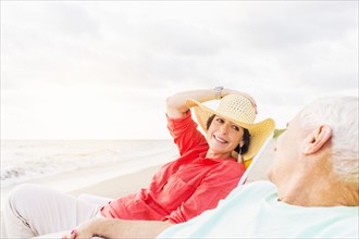 View of couple sitting in lounge chairs on beach