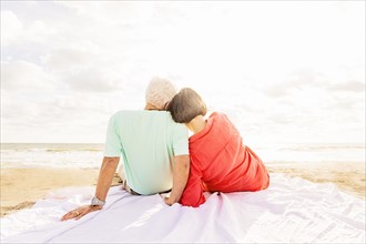 Rear view of couple sitting on beach at sunrise