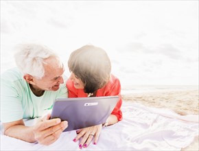 Couple with digital tablet lying on blanket at beach