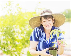 Portrait of smiling woman holding potted plant in garden
