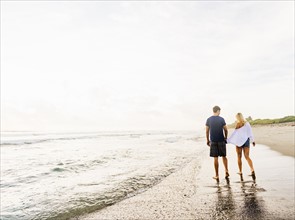 Young couple walking along surf line of sandy beach, holding hands