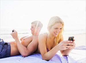 Portrait of young couple relaxing on beach, using smart phones