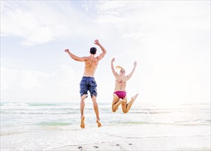 Rear view of young couple jumping on beach