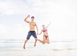 Young couple jumping on beach, holding hands