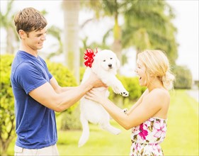 Boyfriend giving white puppy with ribbon bow to girlfriend as present