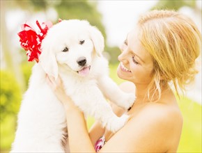 Young woman holding white puppy with ribbon bow