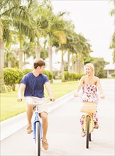 Young couple driving bicycles along street with palm trees