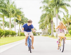 Young couple driving bicycles along street with palm trees