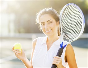 Portrait of young woman holding tennis ball and tennis racket