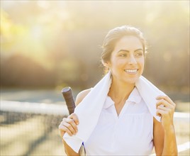 Portrait of smiling young woman with towel and tennis racket