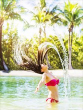 Portrait of young woman wearing bikini tossing hair and splashing water in tropical lagoon