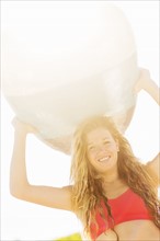 Portrait of young woman holding surfboard over head