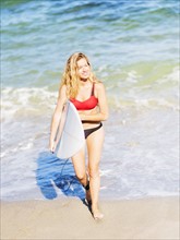 Portrait of young woman walking in surf, carrying surfboard