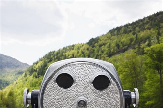 Close-up view of coin-operated binoculars against background of wooded Adirondack Mountains