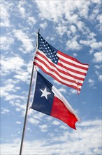American and Texas flags against cloudy sky