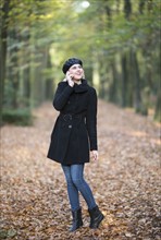 Smiling woman using phone while walking in forest