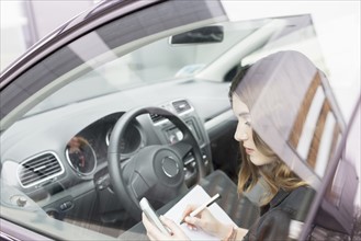 Young woman writing in notebook in car