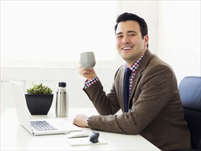 Portrait of businessman sitting in office and drinking coffee