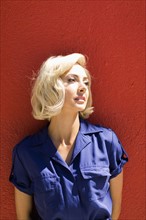 Close-up of Woman in blue dress posing against red wall in sunlight