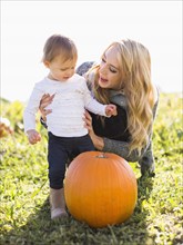 Mother and daughter (12-17 months) looking at large pumpkin