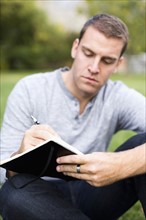 Portrait of young man writing journal in park