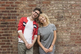 Portrait of couple standing against brick wall.