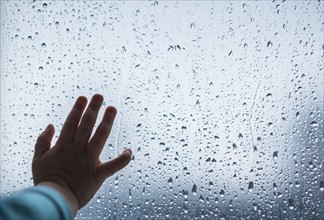 Close-up of girl's hand on wet window.