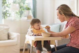 Mother feeding little boy (2-3 years) in high chair.