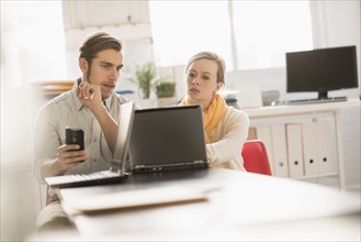 Young man and woman working together with laptop in office.
