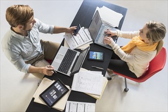 Young man and woman with laptops at desk in office.