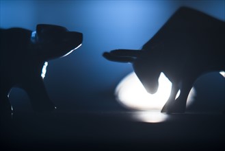Silhouettes of figurines of bull and bear in spot light.