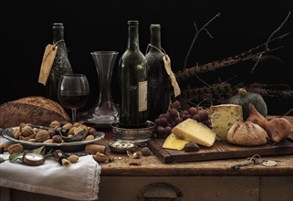 Still life with wine bottles, selection of cheese, bread and nuts on wooden table, studio shot.