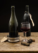 Still life with red wine glass and bottles on wooden table, studio shot.