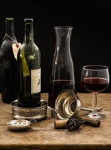 Still life with red wine glass, carafe and bottles on wooden table, studio shot.