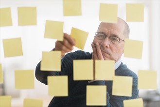Businessman arranging adhesive notes on glass wall.