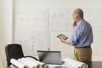 Mature architect looking at blueprints in office.
