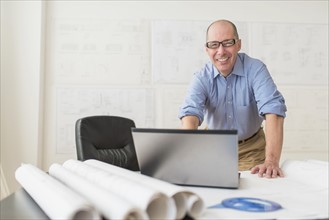 Portrait of smiling mature architect using laptop in office.