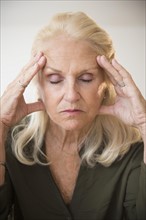 Portrait of senior woman holding head, eyes closed