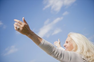 Senior woman with arms outstretched against sky